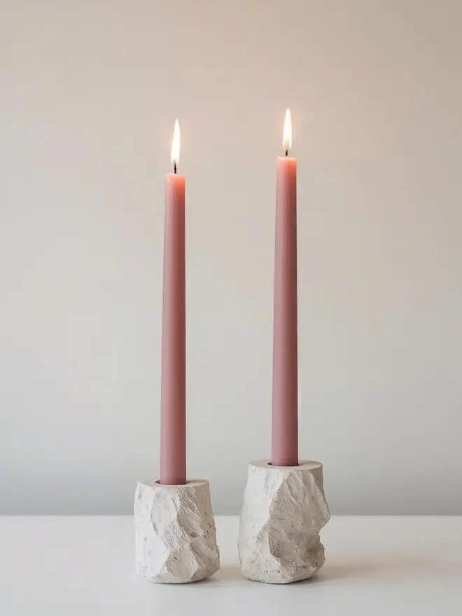 two dusty rose dinner candles in concrete candle holders on a table