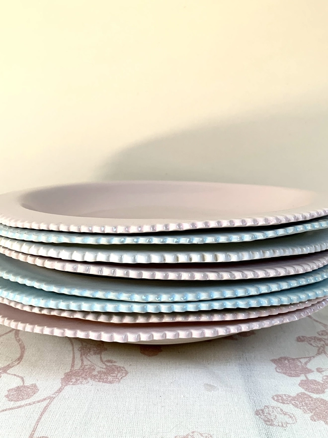 stack of pale pink, white and soft blue pasta bowls showing scalloped edge rims