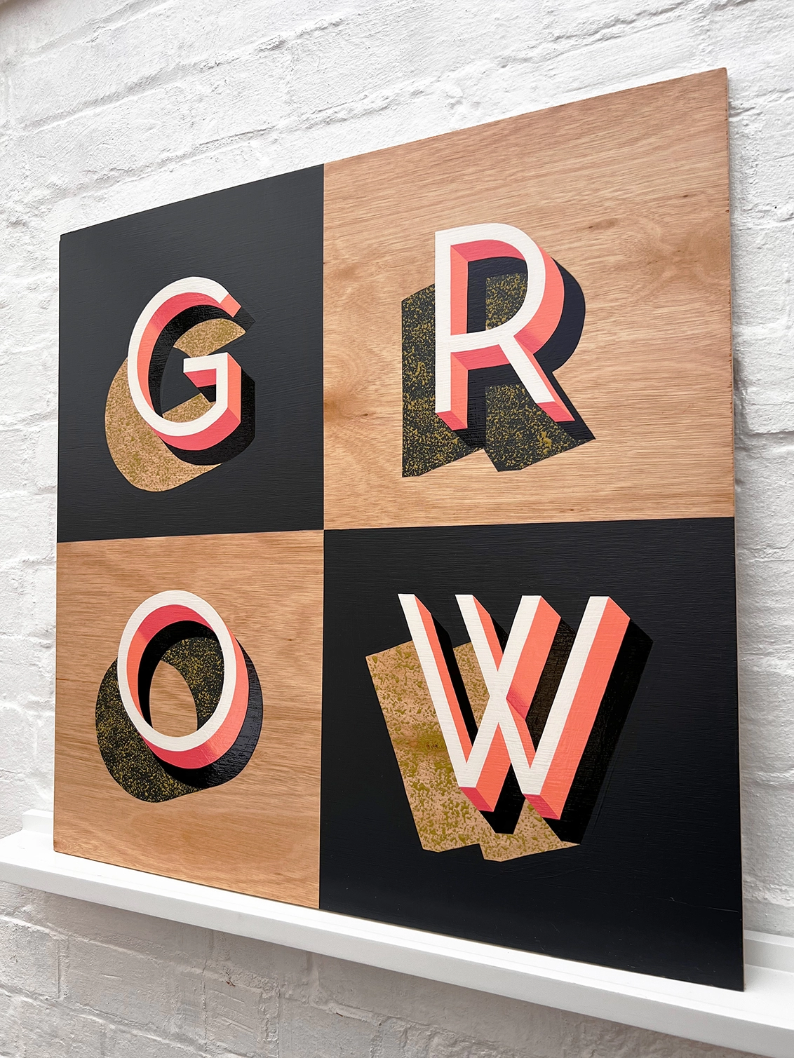 GROW hand painted sign in coral, dark grey and chartreuse, against a white brick wall, at an angle. 