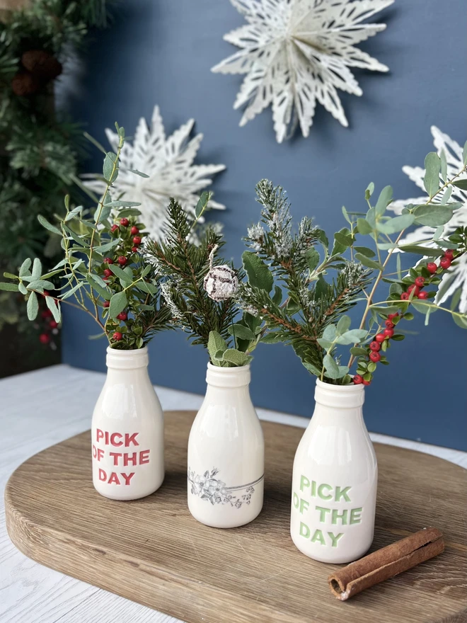 A wild flower bottle between two pick of the day bottles all filled with Christmas Foliage