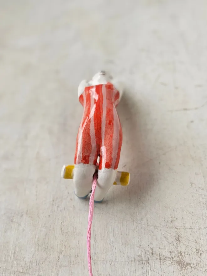 female acrobat hanging upside down in a red and pink stripe suit, front view