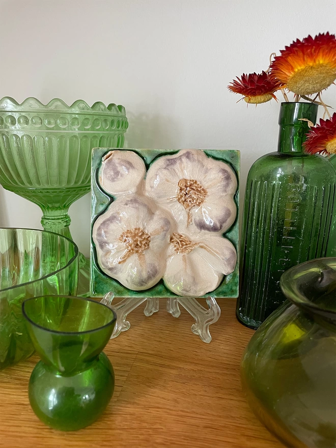 Decorative eye-catching garlic feature tile – three-dimensional, very realistic and incredibly tactile - displayed on a mantelpiece alongside antique green glass.   