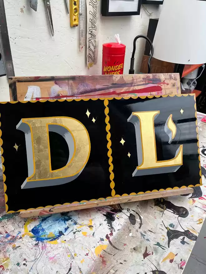 Gold leaf 'D' and 'L' with yellow outline and border and grey shades.