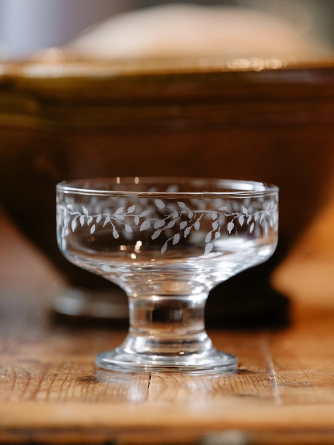 Two clear glass dessert bowls with an etched leaf pattern filled set on a rustic wooden table.