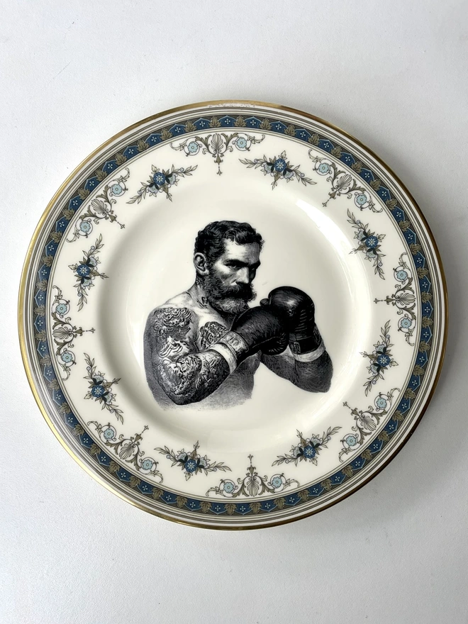vintage plate hanging on a white wall, it has a decorative border, with a printed vintage illustration of a wild beard east end boxer in the middle 