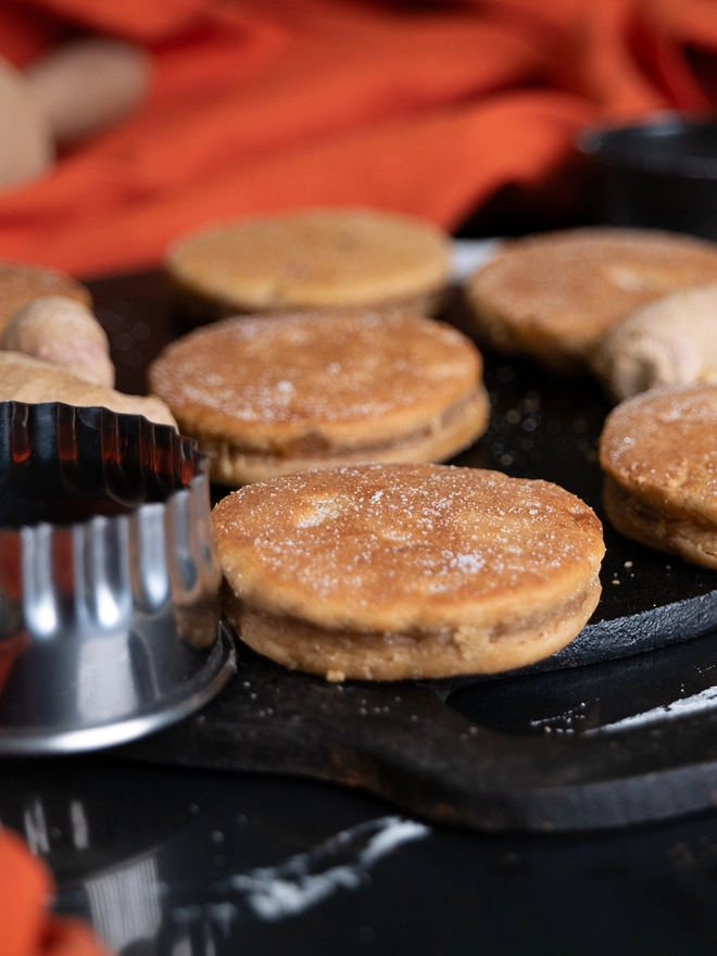 Ginger Welsh Cakes on a black bake stone griddle next to a welsh cake cutter