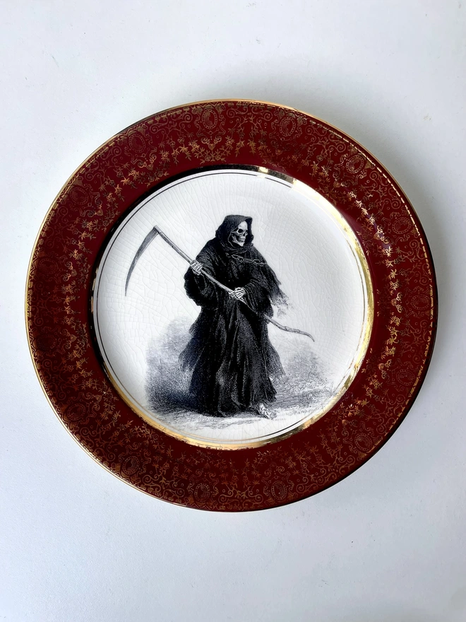 a vintage plate with an ornate border has a vintage illustration in black and white of a grim reaper skeleton in the centre of the plate