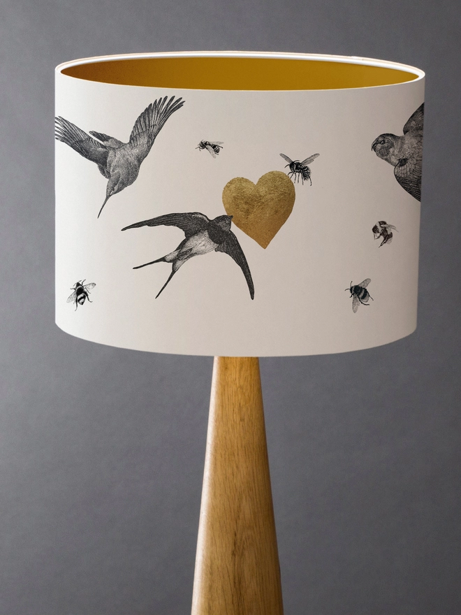 Drum Lampshade featuring birds and bees with a gold heart with a gold inner on a wooden base 