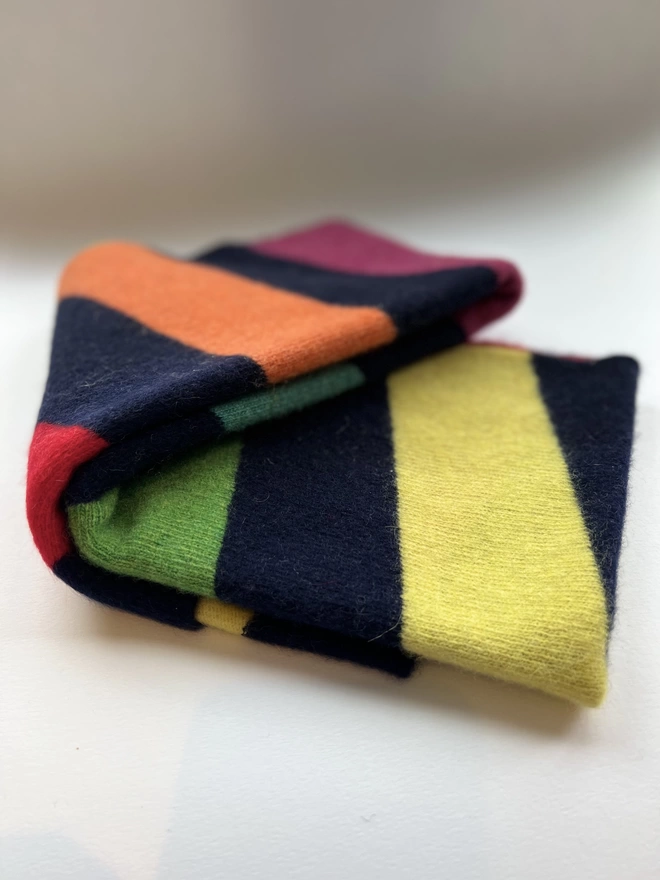 Navy scarf with colourful stripes shown folded and laying flat on white background