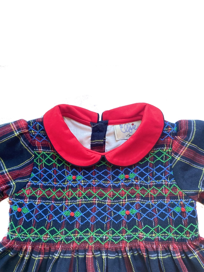 A navy and red tartan dress with a red collar and hand smocking with holly embroidery