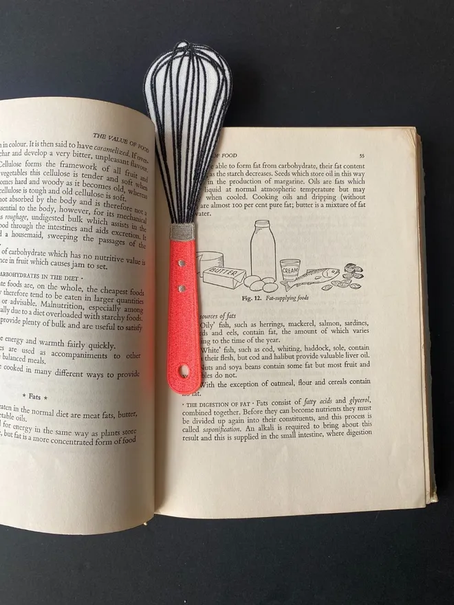 Whisk bookmark inside vintage cookbook markimg a page.