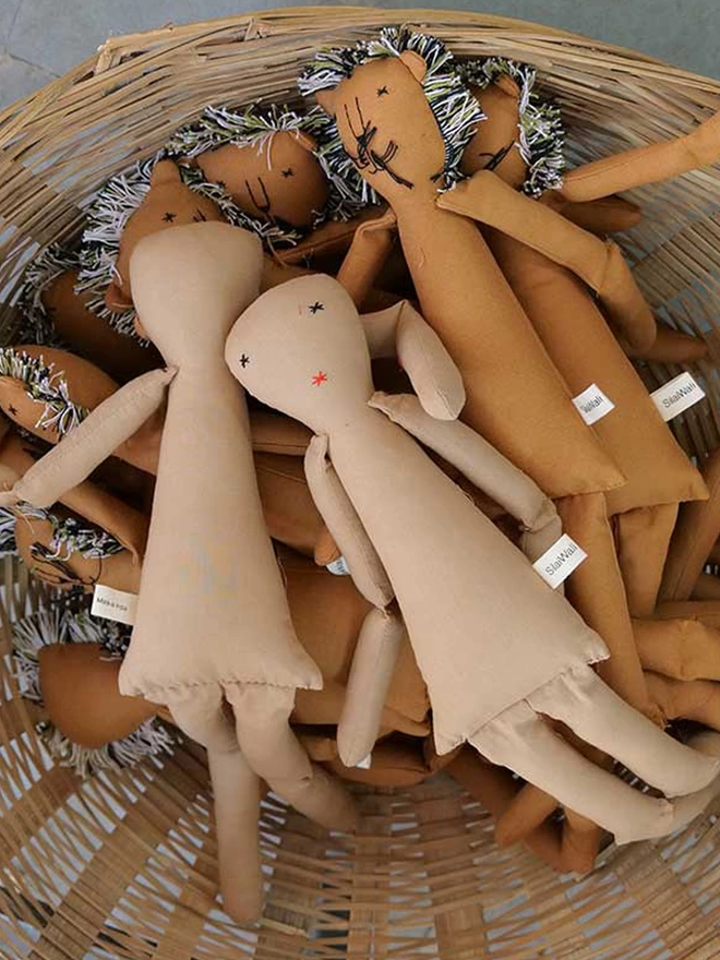 Pile of stuffed dolls shaped like girls and others like lions inside a wicker basket without any outfits 
