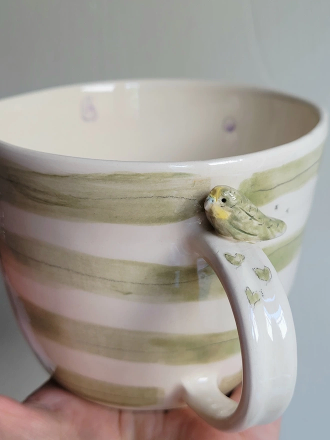 Green stripey cup with a budgie bird, hearts bird prints and lilac spots on the inside 