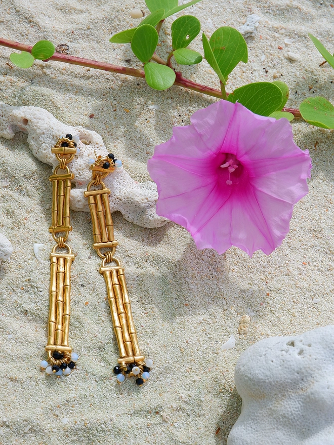 Gold Vermeil Bamboo bar drop earrings with black & white gemstone beads on beach with coral and pink flower