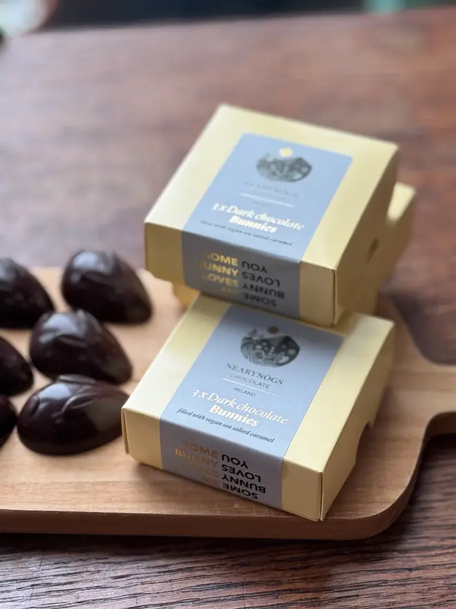 Chocolate Caramel Filled Bunnies 60% (Box Of 3), a stack of chocolate boxes accompanied by chocolate rabbits next to them. 