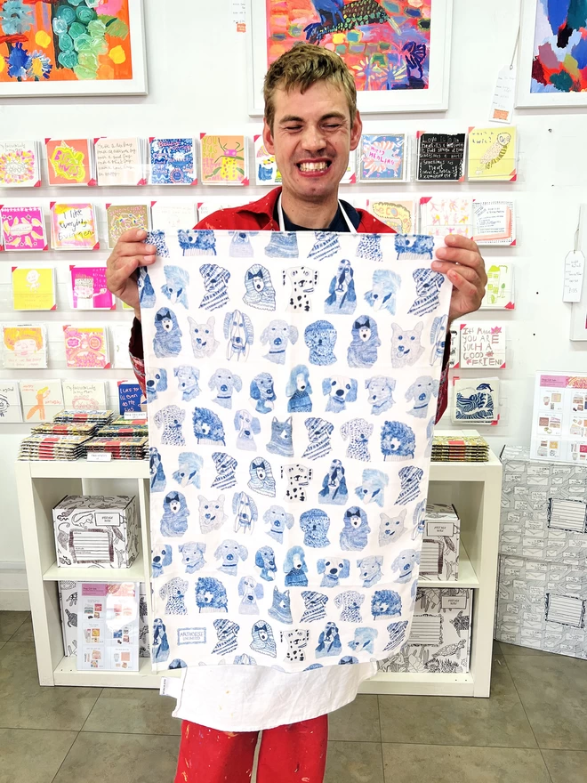 Happy artist holding blue dogs 100% organic cotton charity tea towel illustrated with blue sketched dogs
