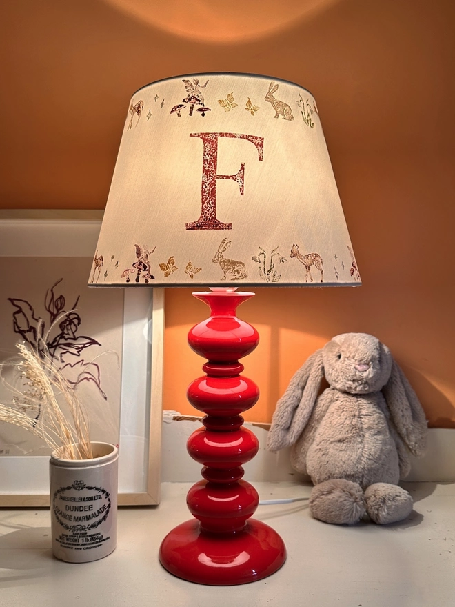 Empire lampshade for kids bedroom with woodland animals and personalised initial, lit to show warm kids lighting. A colourful lampshade and personalised kids gift perfect for bedtime reading.
