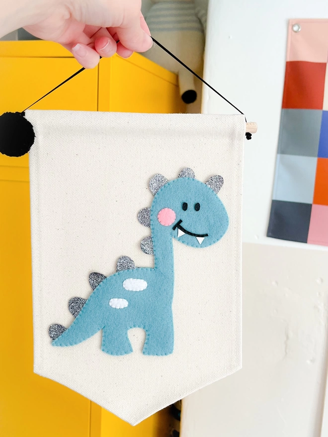 Blue dinosaur with a smiley face on a cream fabric banner