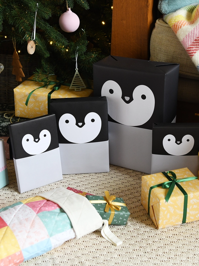 Several gifts wrapped in penguin wrapping paper are on the floor beneath a Christmas tree.