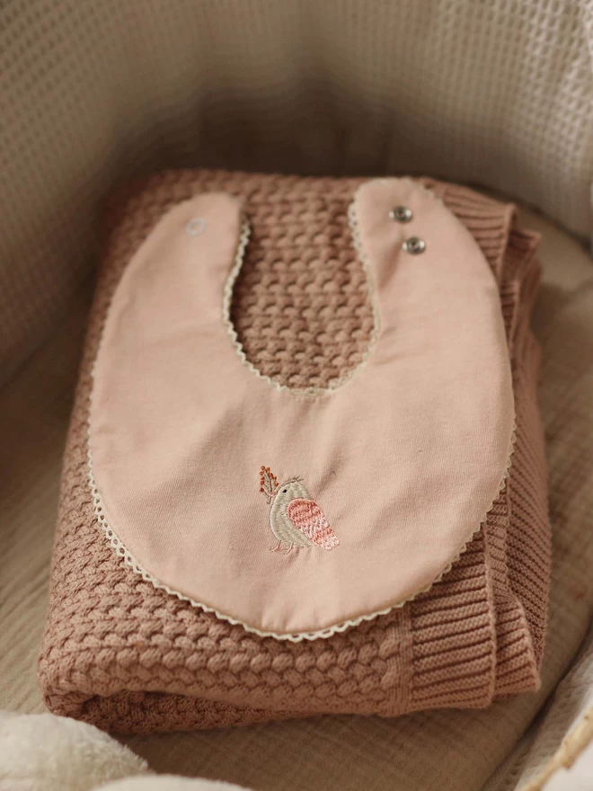 A pink cotton bib with bird embroidered in the middle
