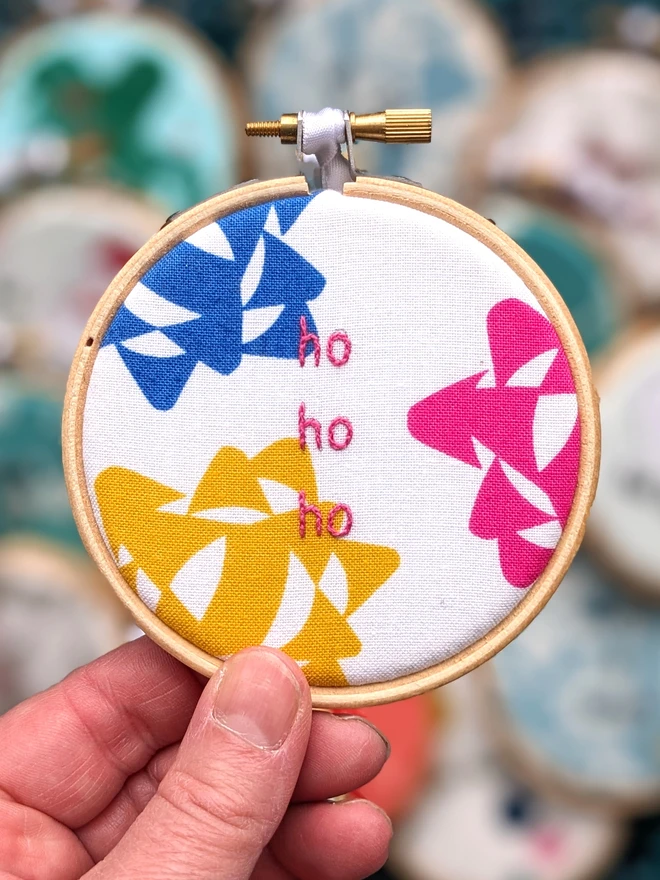 A hand embroidered hoop on Christmas fabric reading ho ho ho