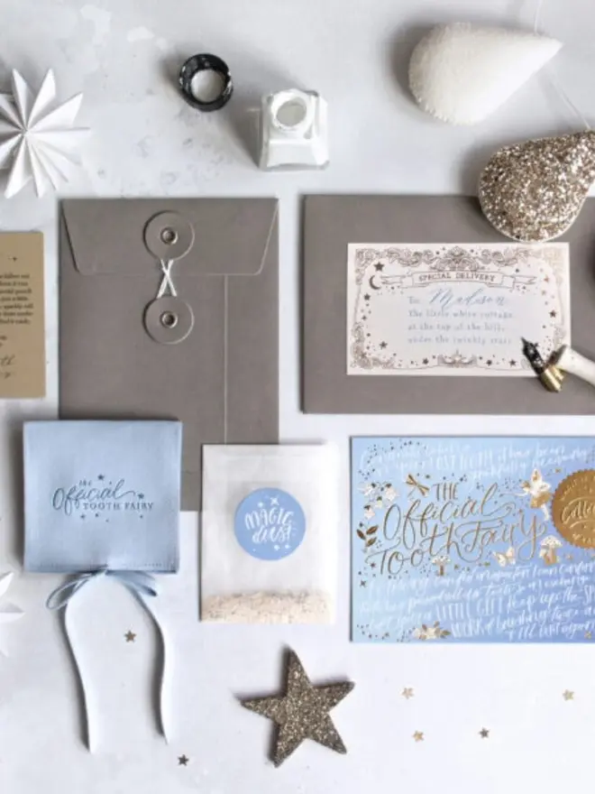 The complete blue set with grey string-tie envelope, Madison's label, pale blue pouch and Magic Dust. A glitter star, an ink bottle and felt teardrops sit around it.