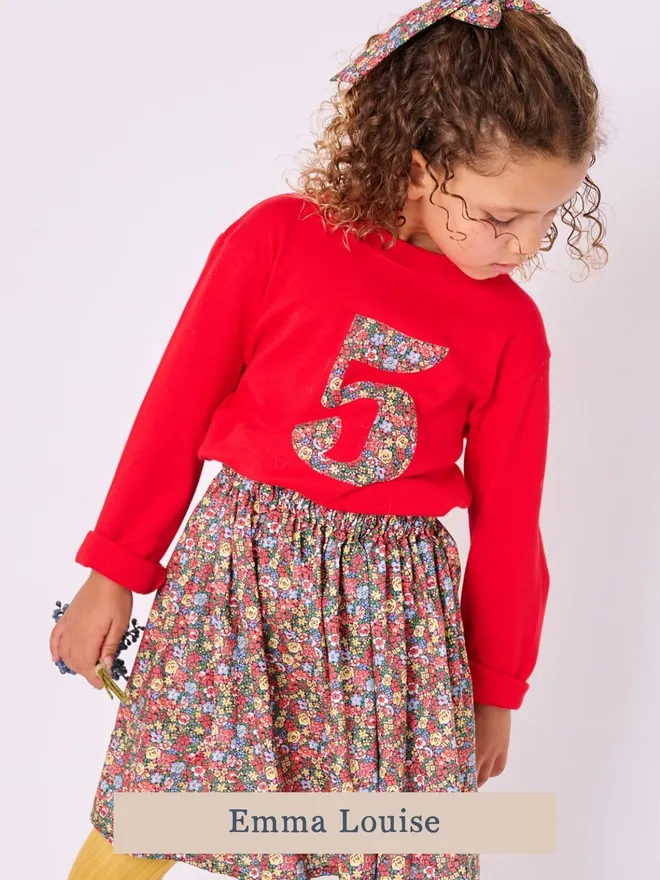 a 5 year old birthday girl wearing a red long sleeve cotton t-shirt appliquéd with a number 5 in floral Liberty print  