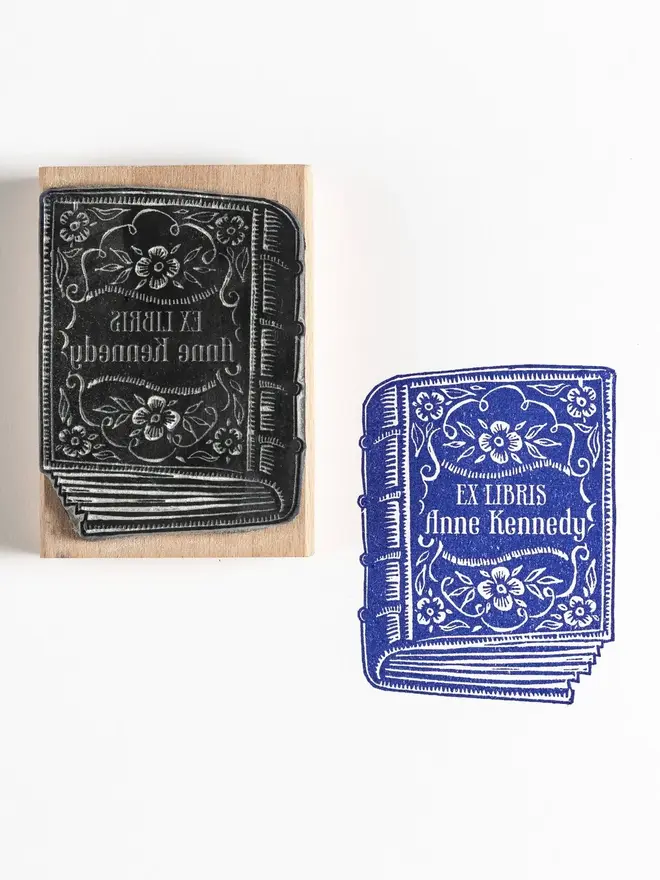 Wooden rubber stamp with an illustrated antique book design, shown next to a blue ink stamped impression reading ‘Ex Libris F. D. Kennedy’.