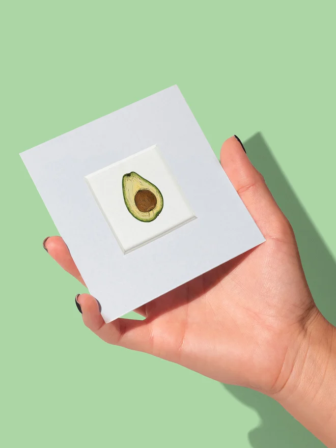Mini art print with mount in hand showing the size of the Avocado tiny print