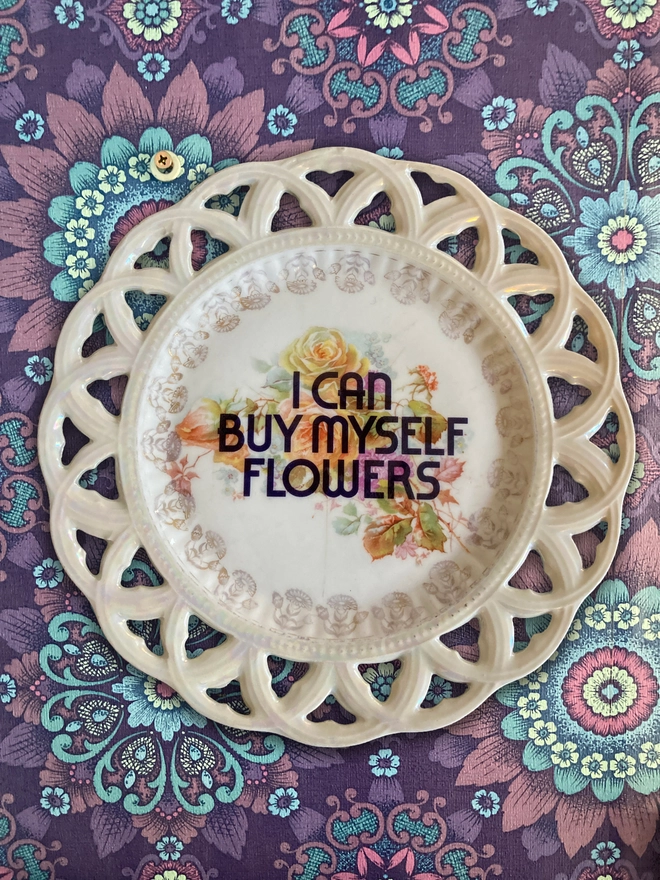 Vintage plate with floral decoration with 'I Can Buy Myself Flowers' in bold type printed over the top.