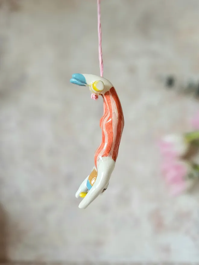 female acrobat hanging upside down in a red and pink stripe suit, side view