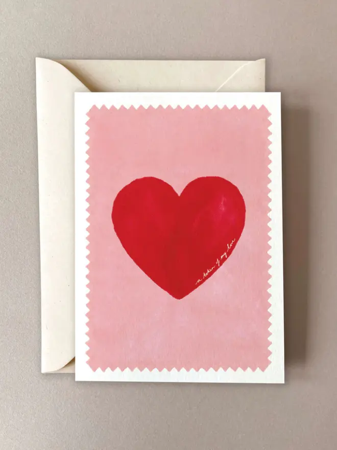 Birthday card featuring a red heart on a  soft pink background with a zigzag edge detail, bordered in white and paired with a matching ivory envelope.