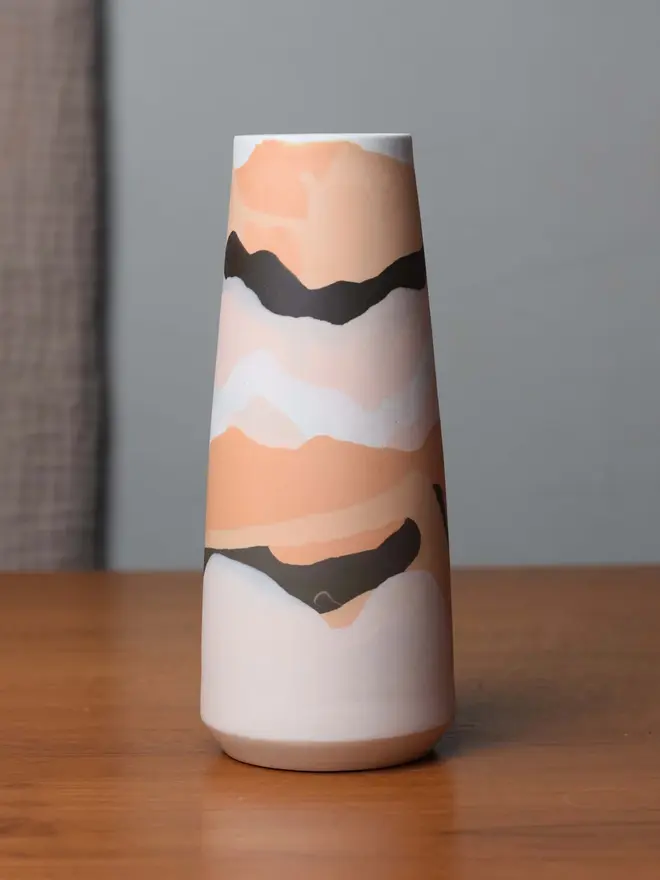 porcelain vase on table, vase has shades of orange, brown, and whites