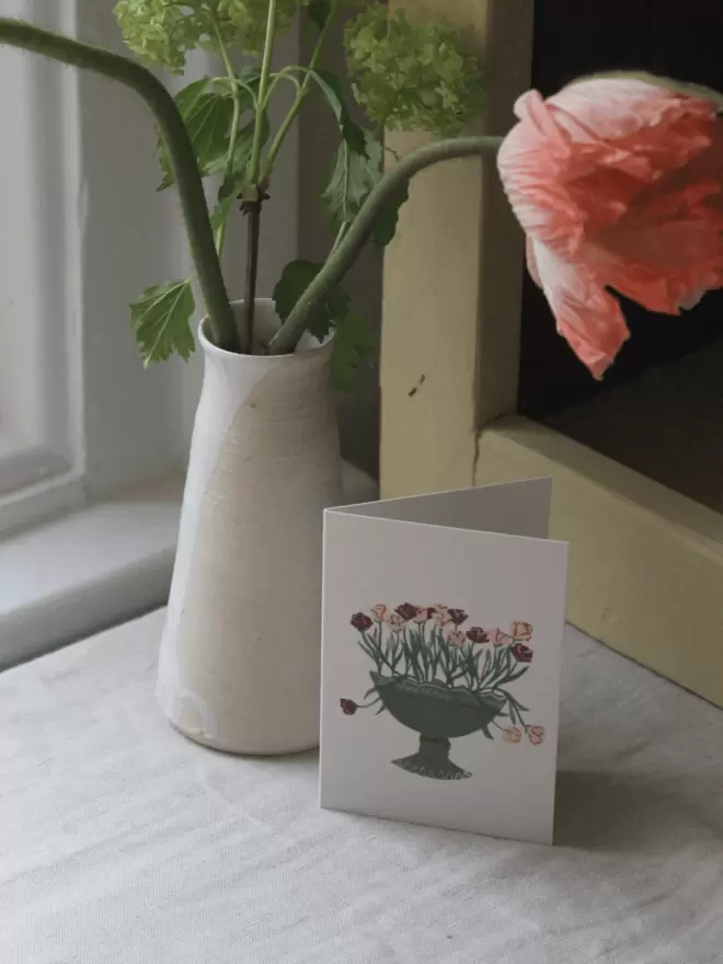 greetings card with parrot tulips and in a green decorative vase next to a vase of icelandic poppies.