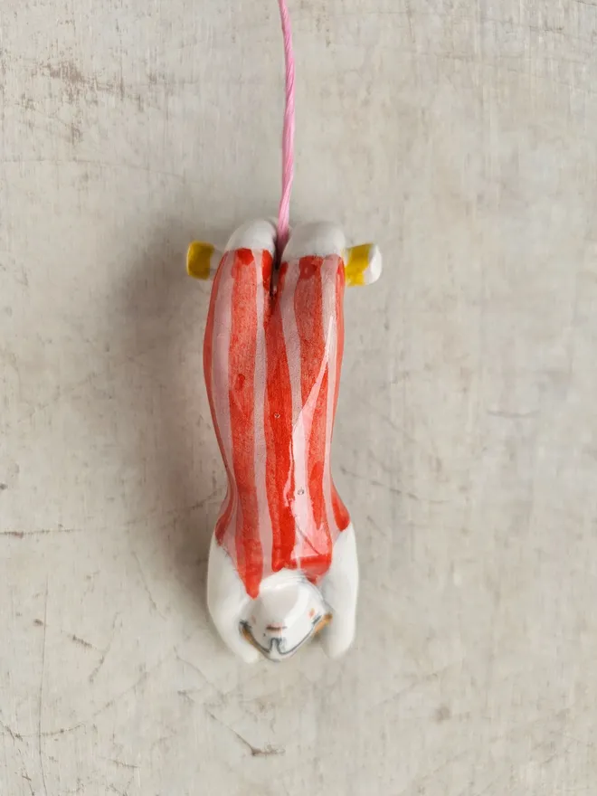 female acrobat hanging upside down in a red and pink stripe suit,front view