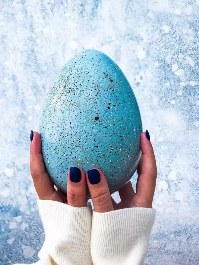 a person holding a blue speckled easter egg in their hands