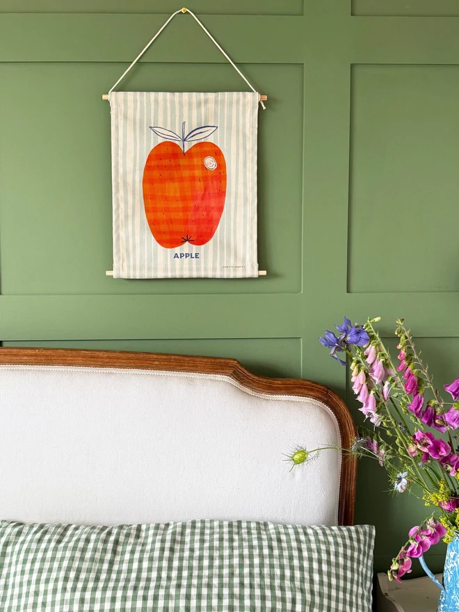 Cotton Apple Wall Hanging, against a green wall. 