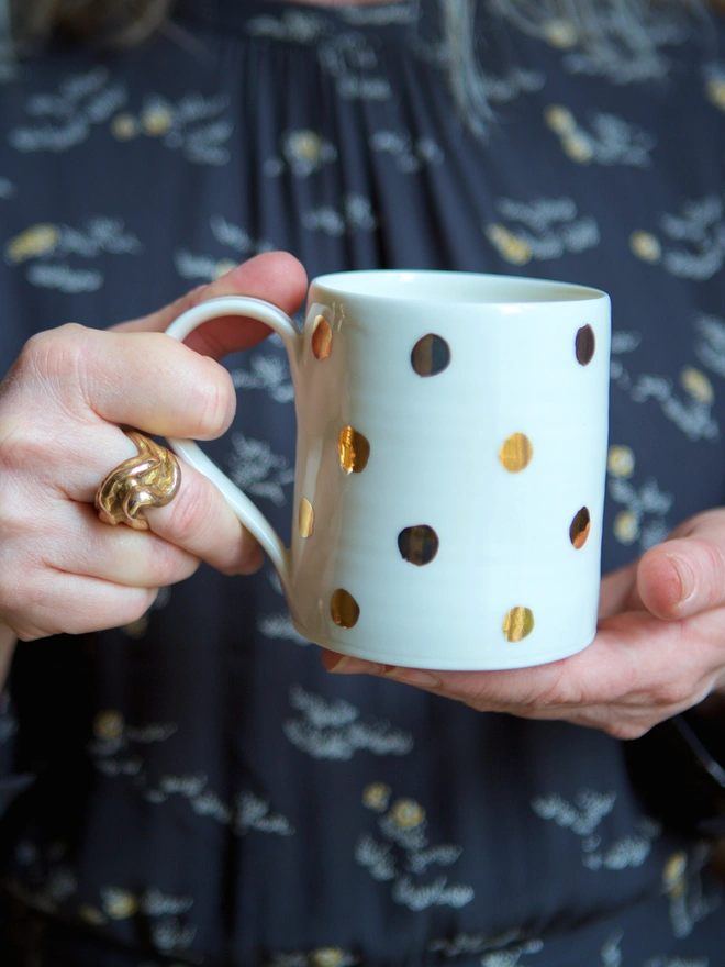 A gold spotted porcelain mug, being held by a woman's hands