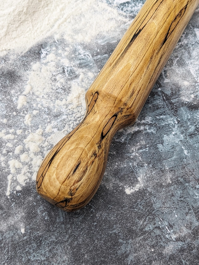  Close up of a stunning hand made rolling pin in Spalted Beech by Something From The Turnery, the picture is focussed on the darker brown all natural detailing along one end of the rolling pin.