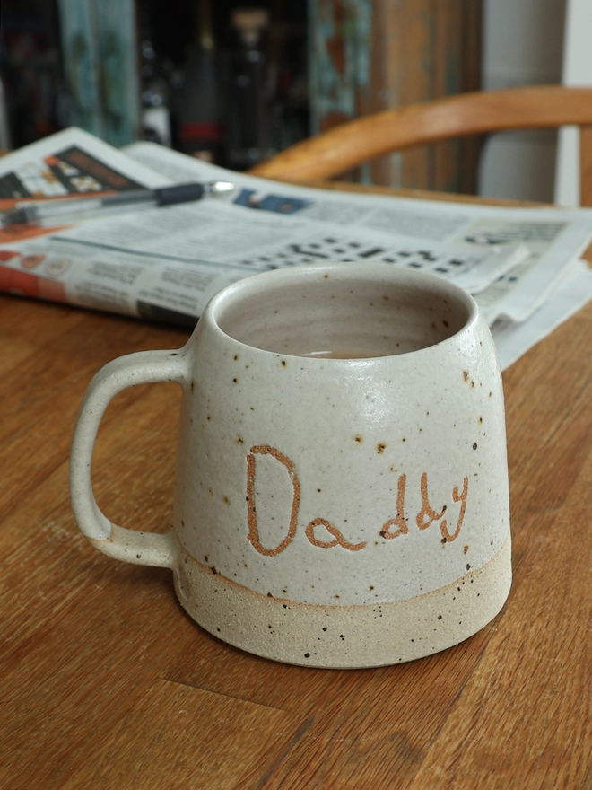 Personalised Kids' Handwriting Handmade Stoneware Mug on table with 'daddy'