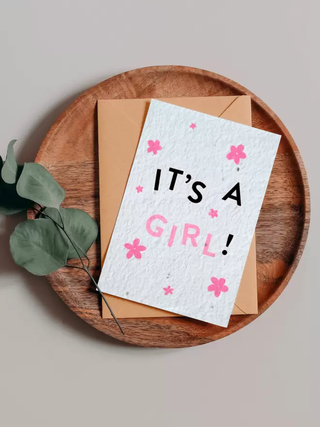 'It's A Girl’ New Baby Plantable Card with Pink Flower Illustrations on a wooden tray next to eucalyptus