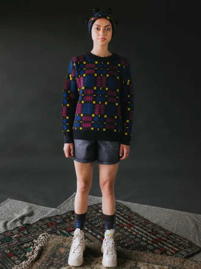 Model wearing pieces from MABLI's 'Carthen' collection, featuring the Carthen Jumper in the vibrant 'Fireworks' colour-way. The design showcases bold, colourful patterns inspired by traditional Welsh blanket tapestry.