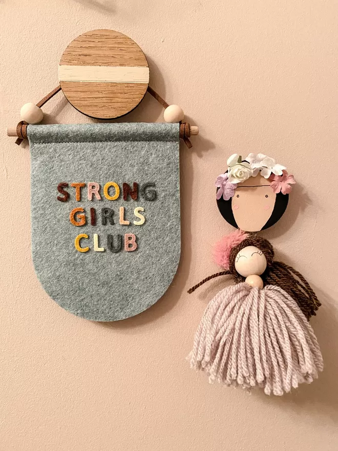 Blue flag saying strong girls club hanging alongside a small tassel doll.